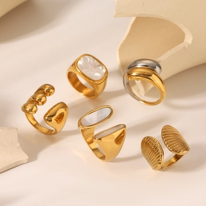 Detailed view of modern stainless steel rings with white shell inlays on beige props