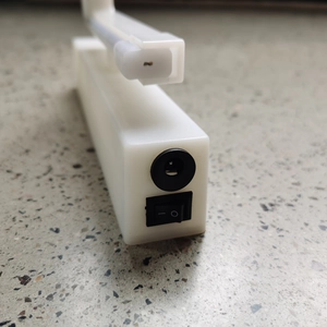 Detail of LED neon base featuring a black power jack and rocker switch on white plastic