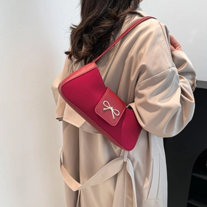 Red PU leather baguette shoulder bag with metal bow detail worn by model in beige coat