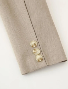 Detail of khaki blazer sleeve showing three amber-toned buttons and woven texture