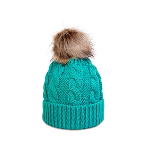 Detailed cable knit pattern on teal winter hat with fluffy faux fur pom-pom topper