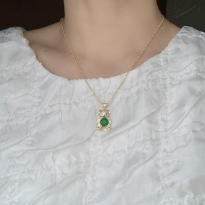Detail view of a gold bead chain necklace with a green gemstone bear pendant on a model