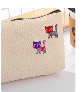 Detailed view of red and purple cartoon cat enamel pins decorated on a beige canvas bag