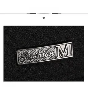 Detailed close-up of a silver Fashion M metal emblem on a black thickened winter flat cap