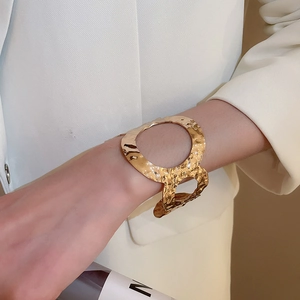 Detail of a wide gold cuff bracelet featuring irregular hammered texture on a model sleeve
