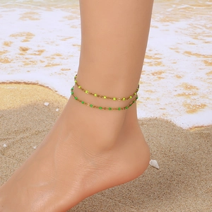 Golden double-layer anklet with neon green beads worn on beach sand for summer vacation