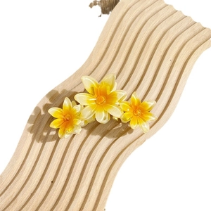 Three gradient yellow plumeria flower hair claws on a wooden display stand for women