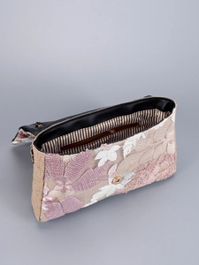 Detail of floral embroidery and sequins on a beige woven shoulder bag with magnetic snap