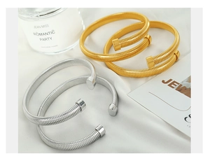 Detailed shot of Tubogas style ribbed open bangles in gold and silver on white silk fabric