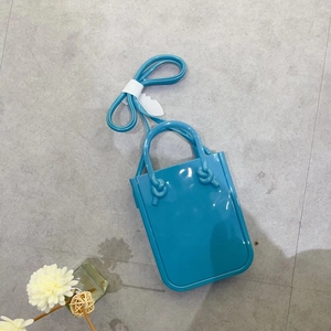 Flat lay of a bright blue PVC jelly handbag with top handles and a long shoulder strap