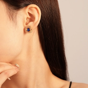 Detail of elegant gold flower earrings with a blue gemstone and pavé diamonds worn by model
