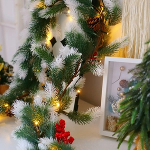 Close-up of frosted Christmas pine needles with red berries, cones and warm LED lights