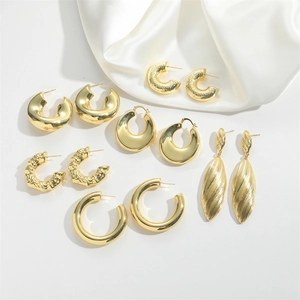 Flat lay of gold hoop and textured earrings on white silk for a minimalist jewelry look