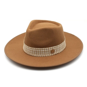 Detail of a brown fedora hat with tweed band and circular metal M logo badge