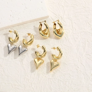 Detail of C-shaped metal hoop earrings with heart charms in gold and silver finish
