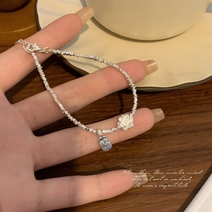 Detail of silver chain bracelet featuring a 3D flower charm and a Fu character pendant
