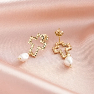 Gros plan de boucles d'oreilles croix dorées et perles baroques sur fond de soie rose