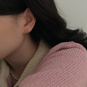 Close-up of elegant gold heart-shaped stud earrings worn with a pink cardigan