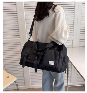 Rear view of model carrying a black nylon travel bag with wide detachable shoulder strap