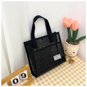 Detail of black mesh tote bag with wide handles and white label on plaid tablecloth