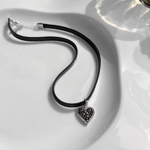 Detail of a dark goth heart choker with crystals in a white ceramic dish