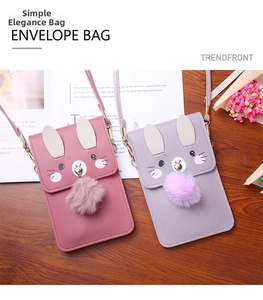 Close-up of pink and purple rabbit-shaped phone bags with soft fur balls on wooden desk