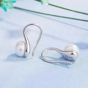 Macro shot of S925 silver pearl drop earrings on a light blue fabric background