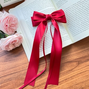 Detail of red satin ribbon bow hair clip placed on a vintage book with roses