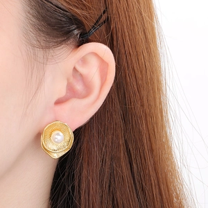 Detail of flower-shaped golden stud earrings with white pearl worn by a model