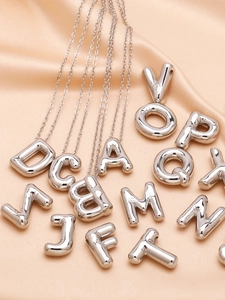 Detailed view of silver balloon initial necklace on champagne silk background