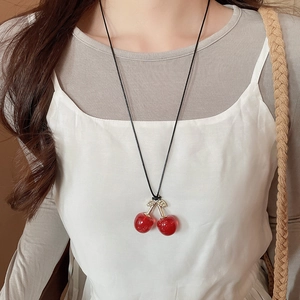 Detail of red cherry pendant necklace with gold leaves on black cord worn by model