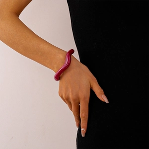 Macro shot of wavy burgundy resin cuff bracelet worn over a black knit sleeve