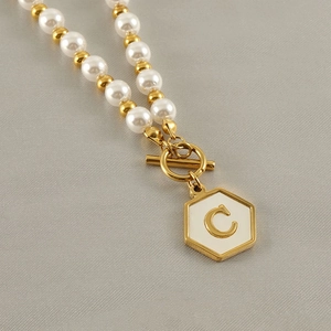 Close-up of pearl necklace with hexagonal C-letter pendant and golden OT toggle clasp