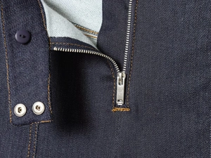 Gros plan sur la fermeture éclair en métal et coutures orange sur veste en jean bleu foncé