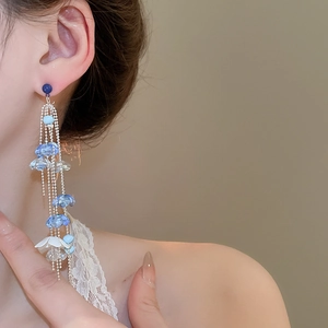 Detail of long floral tassel earrings with blue beads and white acrylic petals on a model