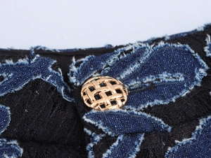 Detail of vintage black lace trousers with blue denim patchwork and golden braided button