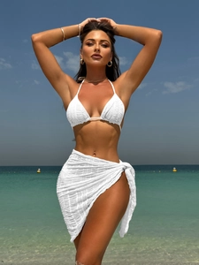 Close-up of white three-piece bikini set with textured fabric and matching sarong on beach