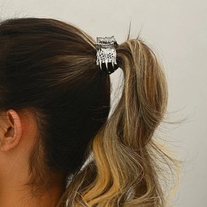 Detail view of a silver metal claw clip styling a high ponytail with elegant texture