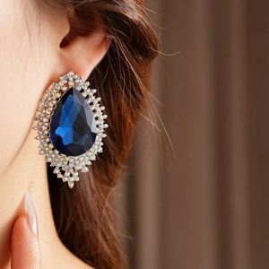 Close-up of deep blue teardrop gemstone earrings with pavé diamond-set borders