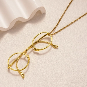 Gold vintage eyewear pendant necklace on minimalist beige textured backdrop