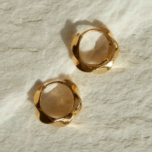 Detailed view of textured gold hoop earrings with irregular wavy design on stone background