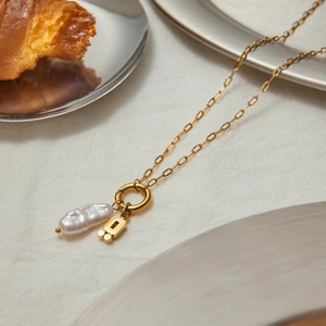 Detail of gold paperclip chain necklace with baroque pearl and geometric pendant charms