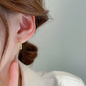 Close-up of elegant interlocking gold geometric rectangular drop earrings on model's ear
