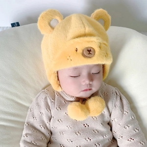 Dettaglio del cappello in peluche giallo per neonati con orecchie da orso e pompon in morbida pelliccia