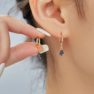 Elegant gold earrings with purple teardrop gemstones and cubic zirconia on model