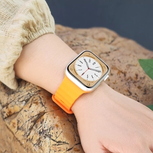 Close-up of vibrant orange silicone wave strap on a silver smartwatch worn outdoors
