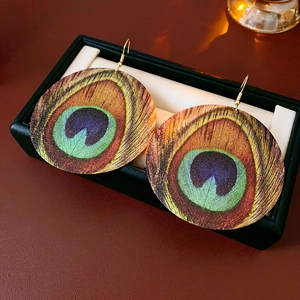 Detail of round peacock feather pattern earrings in a black gift box on a leather surface
