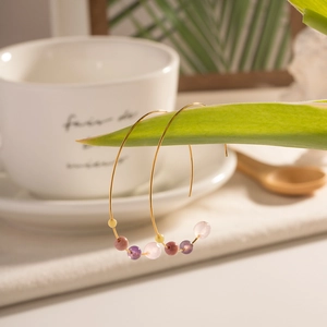 Detailed shot of C-shaped gold earrings with pink, purple and yellow stone beads