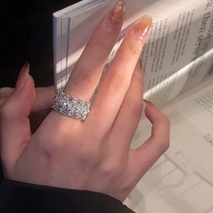 Lace hollow silver ring with zircon stones shown on hand over an open book