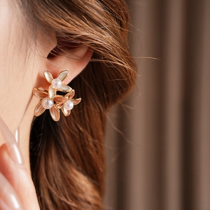 Detailed view of floral pearl earrings with gold plating and pearlescent petals on a model